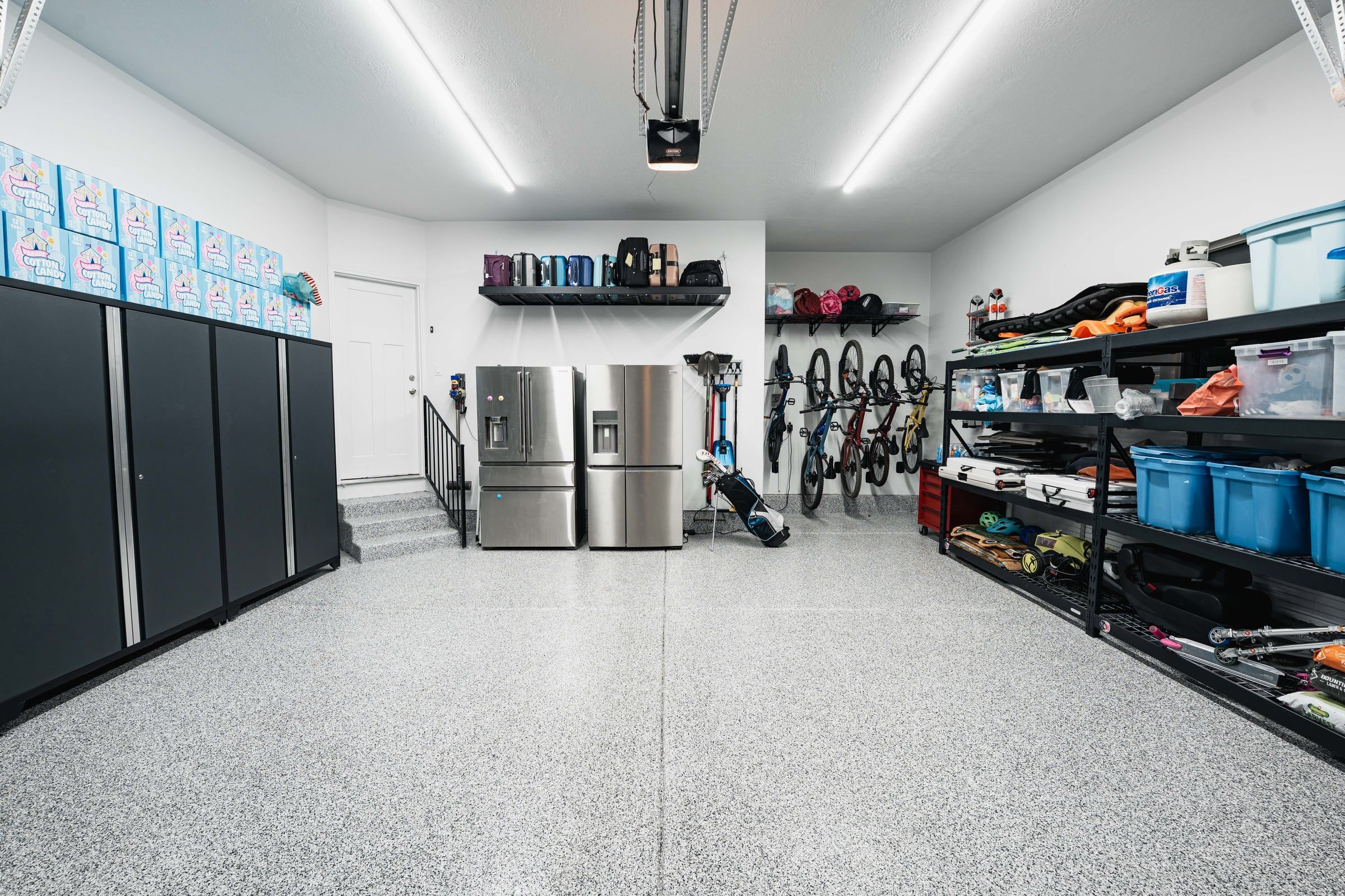 Family garage with black cabinets, open shelving, bikes on hooks and a flake floor