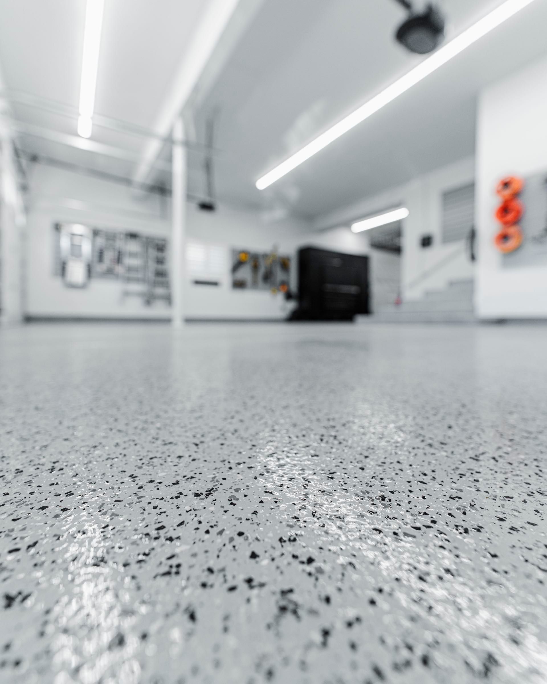 Low view across a glossy light grey flake floor in a bright garage with LED strip lights and black cabinets at the back