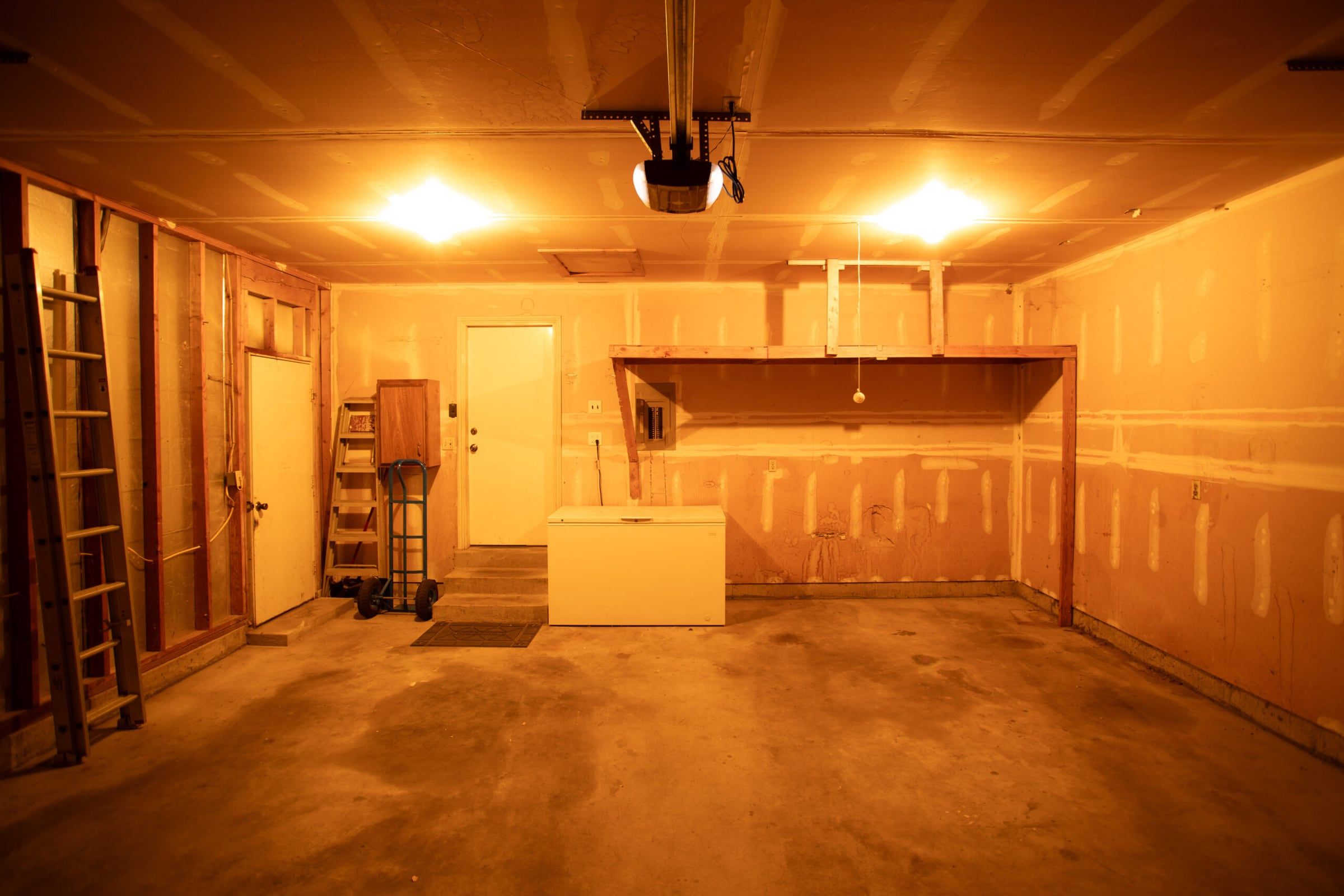Before: unfinished garage with bare drywall, a stained concrete floor and orange work lights